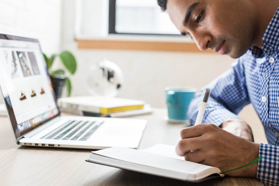 Un hombre sentado en un escritorio escribiendo en una libreta.