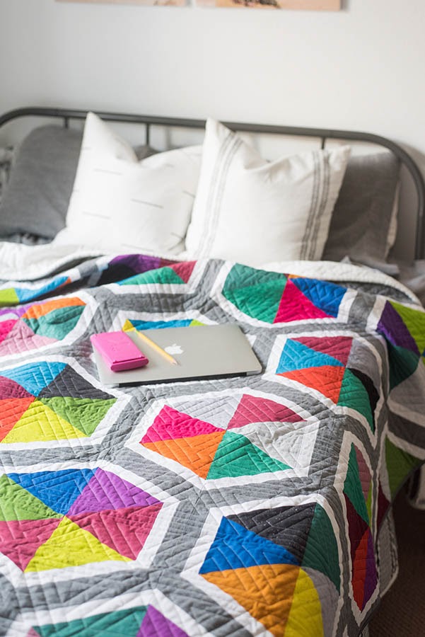 Bed with bright colorful quilt and laptop on top of bed.