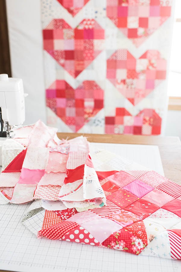Scraps of heart quilt pattern fabric on cutting board near sewing machine.