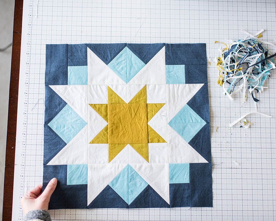 Hand touching quilt pattern with blue sun triangle pattern on cutting board.